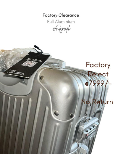Silver suitcase with a tag labeled 'Factory Reject' on a white background